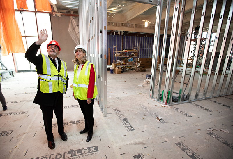 Man and woman in hard hats and construction vests look up in int