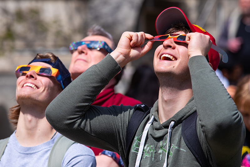 Males wear paper glasses to look at sky 