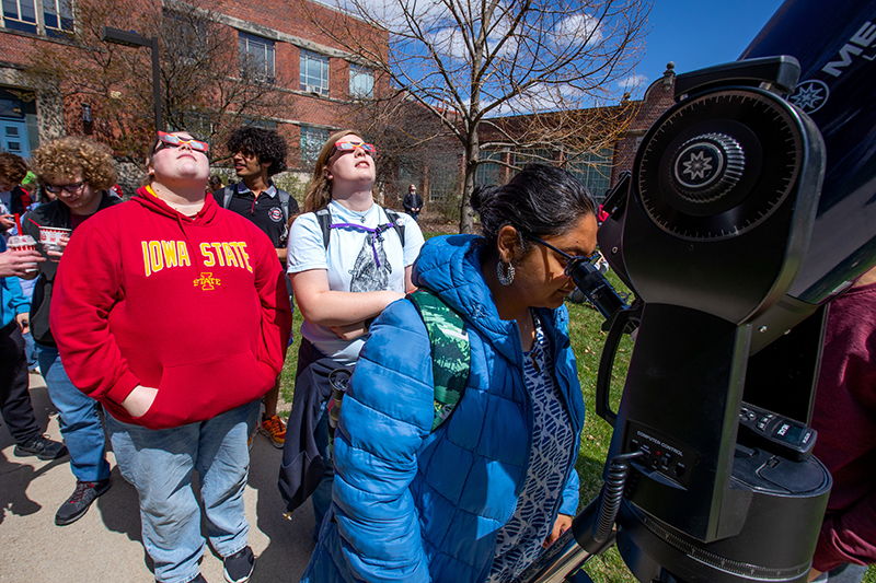 Indian female looks into telescope eyepiece, line of students be