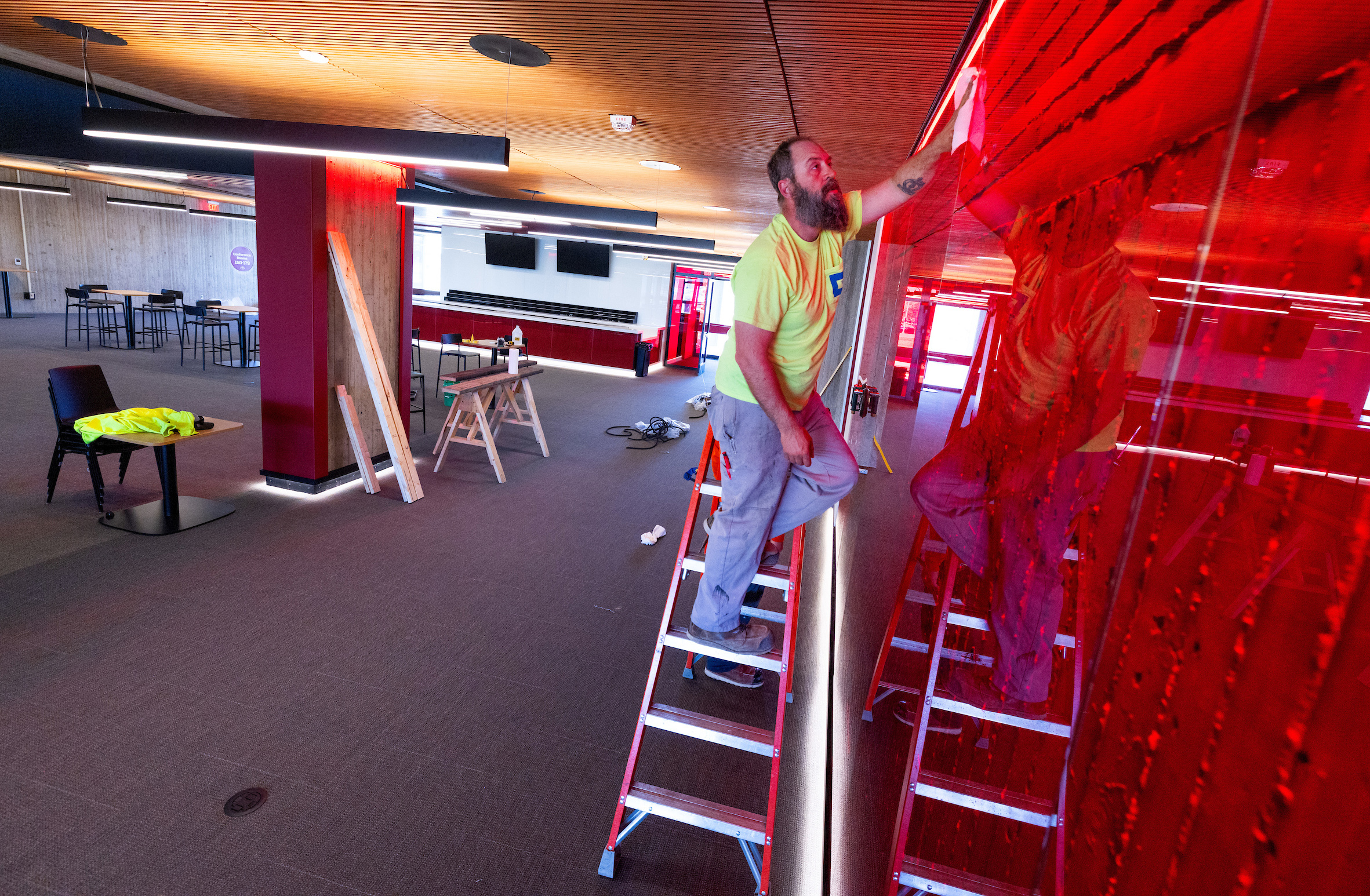 Man with beard on ladder cleans red glass wall in large lounge